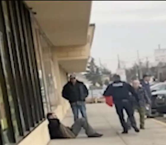 homem sentado em calçada sendo preso por policiais